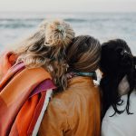 three women are sitting on a bench looking at the ocean