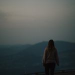 a woman standing on top of a hill looking at the sky